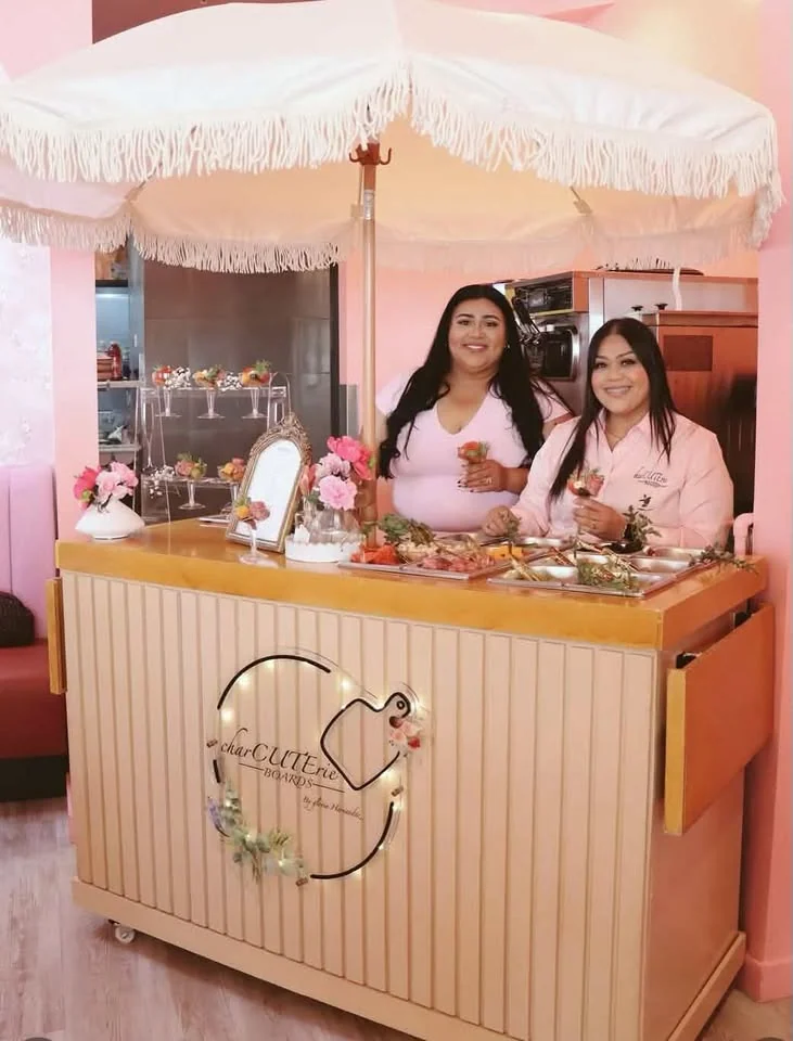 Two women smiling behind a charcuterie service counter