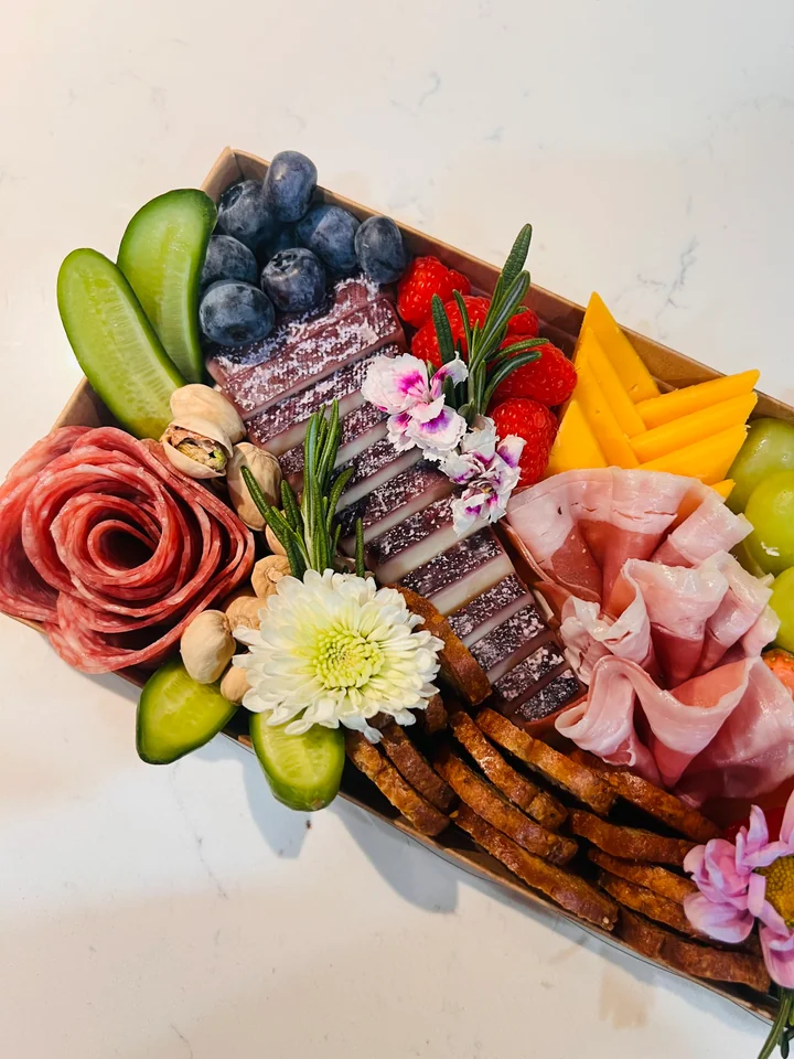 Petite charcuterie board with berries, cucumber, cheese, and flowers