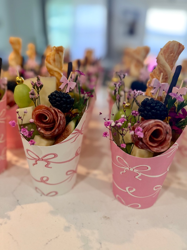 Close-up of pink bow charcuterie cups with salami roses, berries and flowers