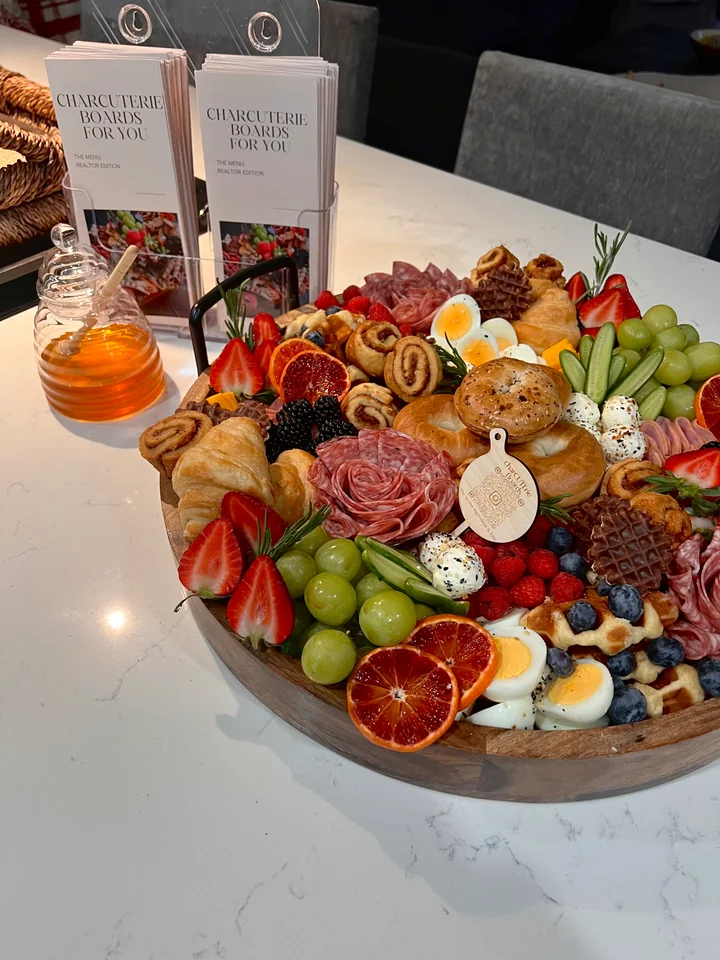 Round event charcuterie board with fruit, cheese, cured meats, and croissants