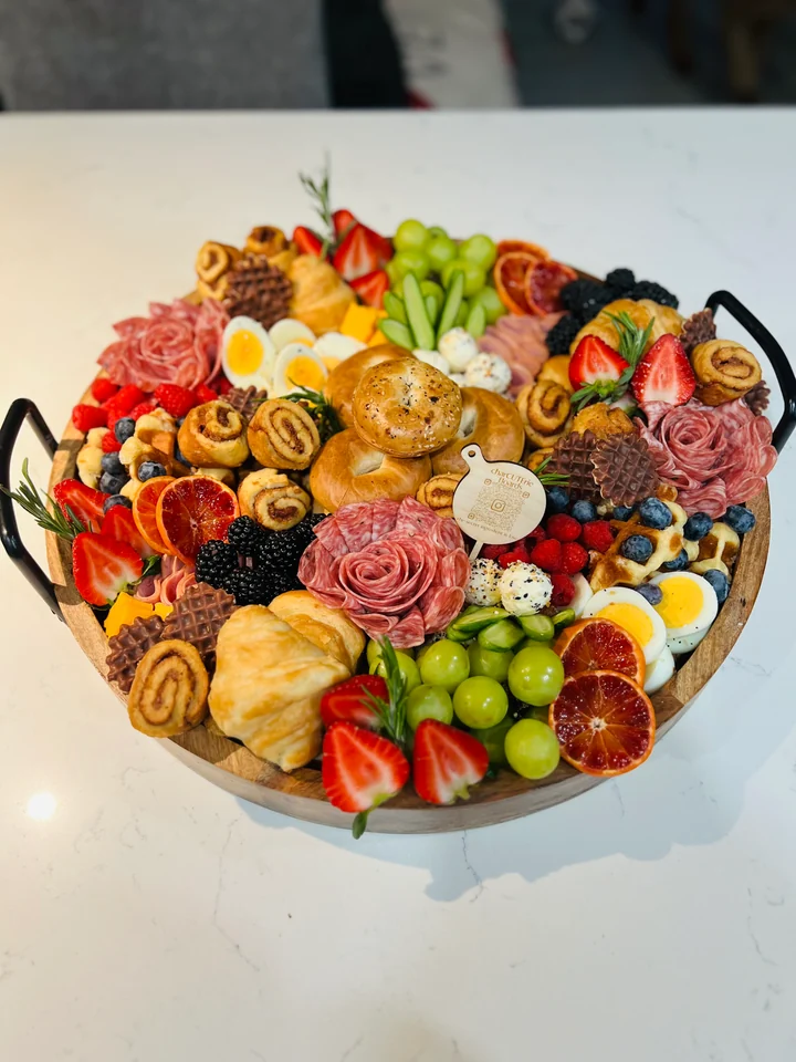 Round charcuterie board with fruit, cheeses, salami roses, and dried citrus